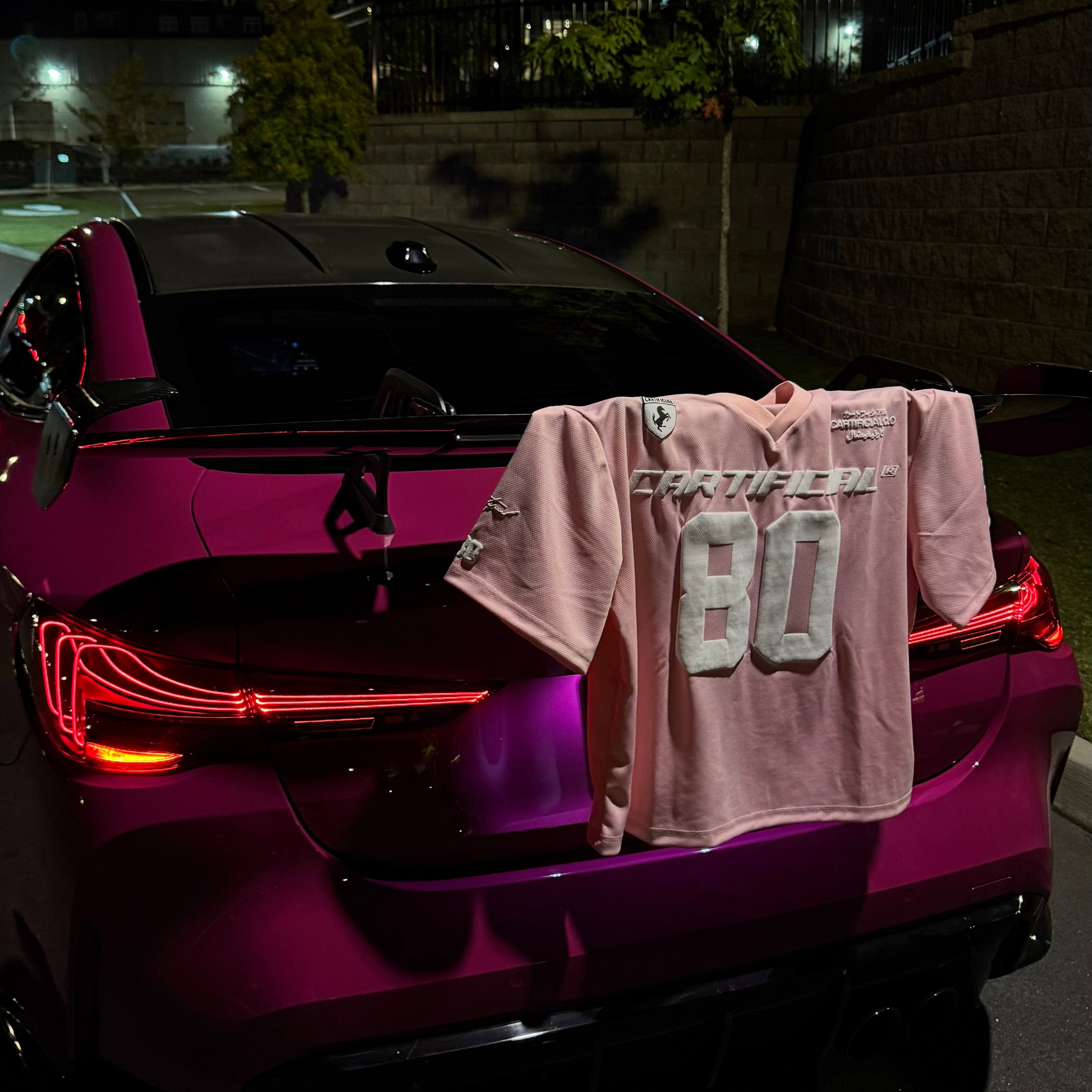 Pink sports car with a jersey hanging from its rear, at night.